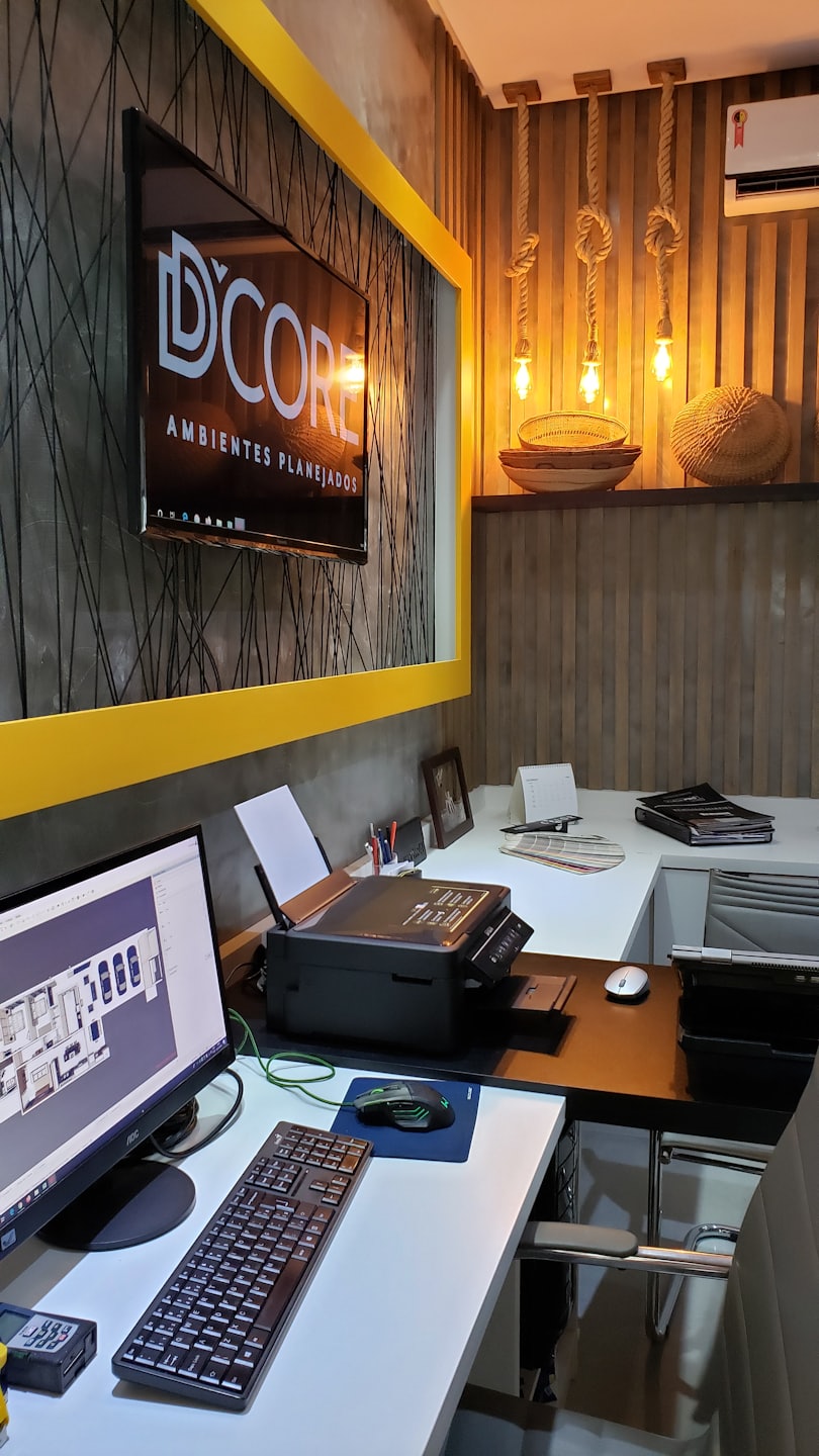 Ufficio moderno con scrivanie, computer che mostrano planimetrie e logo D'CORE.